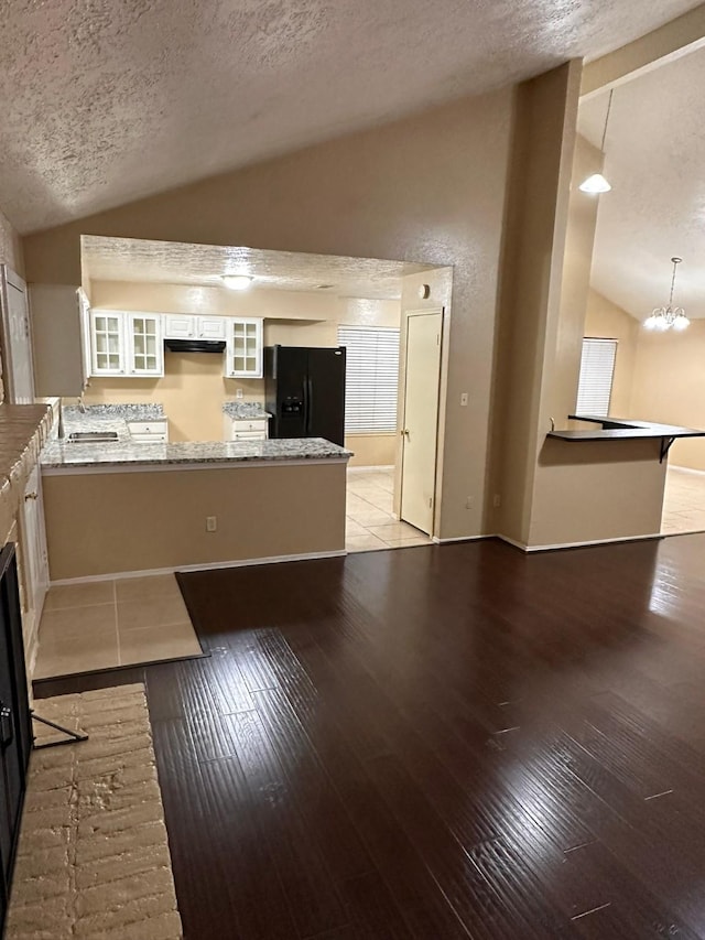 kitchen with black refrigerator with ice dispenser, vaulted ceiling, a textured ceiling, white cabinetry, and kitchen peninsula