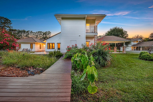 back house at dusk with a balcony and a lawn