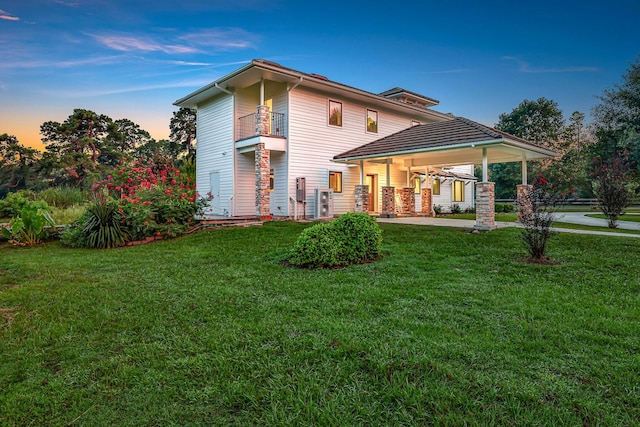 back house at dusk featuring a lawn and a balcony