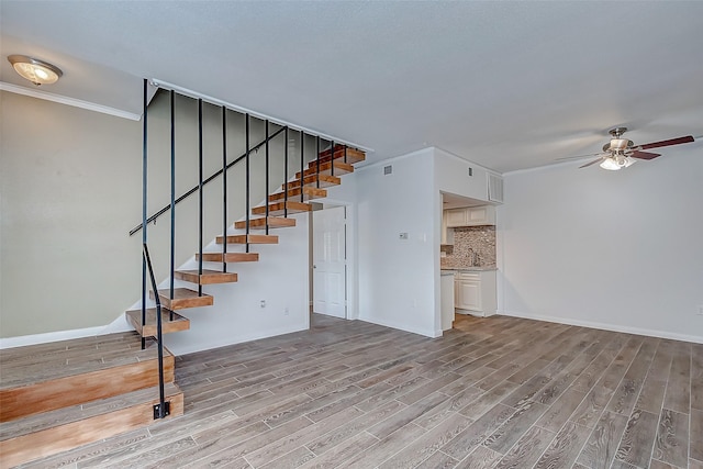 unfurnished living room with light wood-type flooring, ceiling fan, and ornamental molding