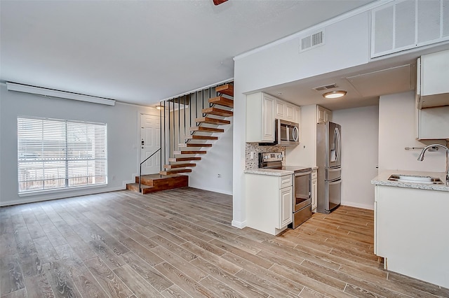 kitchen with decorative backsplash, light wood-type flooring, stainless steel appliances, sink, and white cabinetry