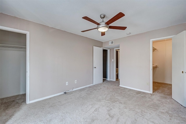 unfurnished bedroom with a walk in closet, ceiling fan, and light carpet