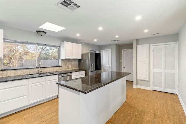 kitchen with a skylight, white cabinetry, sink, a center island, and stainless steel appliances