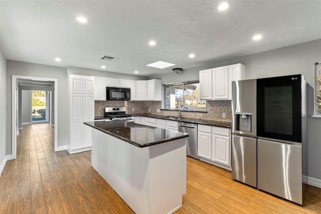 kitchen with a center island, sink, stainless steel appliances, dark stone countertops, and white cabinets