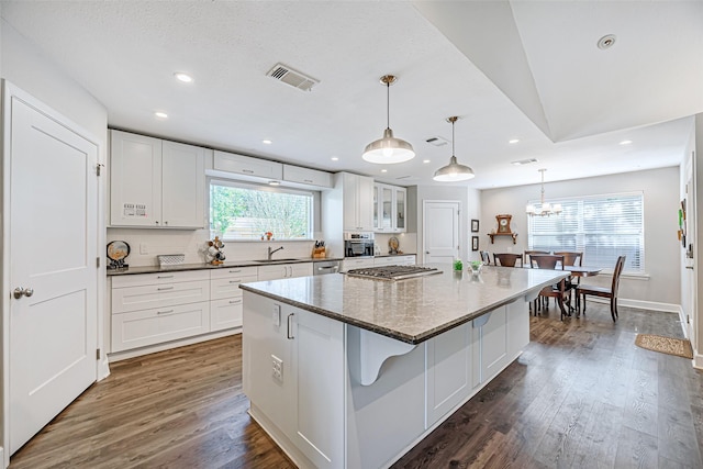 kitchen featuring a breakfast bar, dark wood-type flooring, white cabinets, a kitchen island, and hanging light fixtures