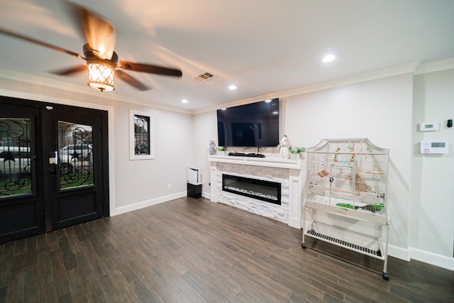 living room featuring dark hardwood / wood-style flooring, a stone fireplace, ceiling fan, and crown molding