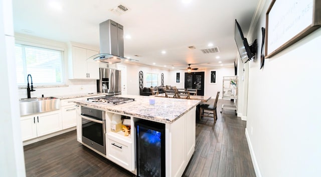 kitchen featuring a center island, white cabinetry, island exhaust hood, beverage cooler, and stainless steel appliances