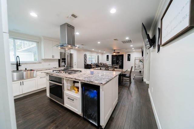 kitchen with island exhaust hood, stainless steel appliances, sink, white cabinets, and a center island