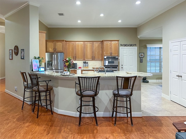 kitchen with stainless steel appliances, ornamental molding, light stone countertops, and a kitchen breakfast bar