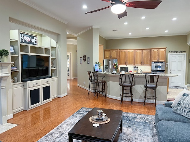 living room featuring built in shelves, light hardwood / wood-style flooring, ceiling fan, and ornamental molding