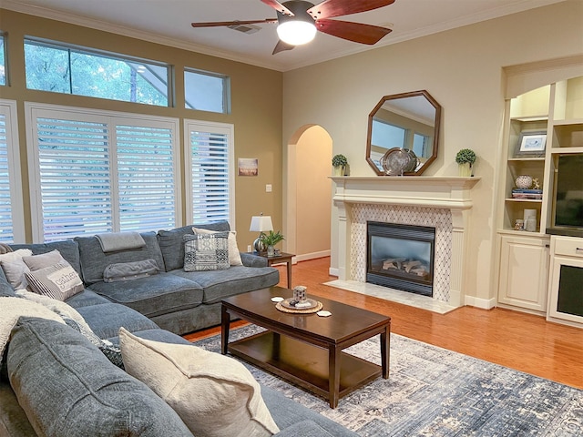 living room with crown molding, a tiled fireplace, wood-type flooring, and ceiling fan