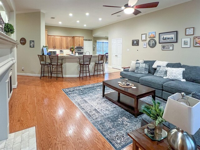 living room featuring crown molding, a tile fireplace, light hardwood / wood-style floors, and ceiling fan