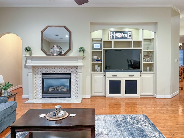 living room featuring built in features, hardwood / wood-style floors, ornamental molding, and a tiled fireplace