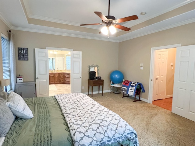 bedroom featuring ensuite bath, light carpet, ceiling fan, a tray ceiling, and crown molding