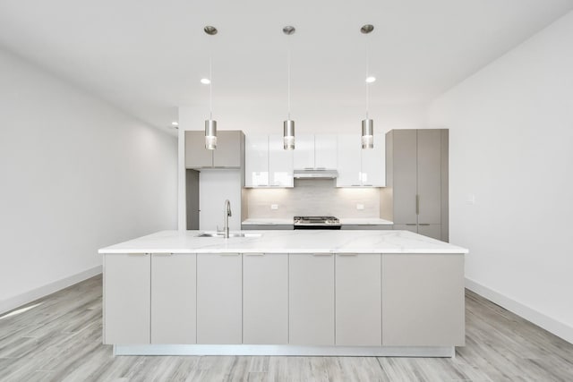 kitchen with light stone countertops, sink, hanging light fixtures, and a kitchen island with sink