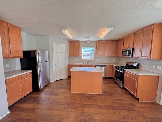 kitchen with appliances with stainless steel finishes, a textured ceiling, dark wood-type flooring, sink, and a center island