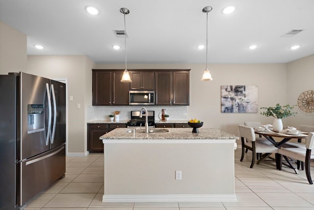 kitchen with pendant lighting, light stone counters, stainless steel appliances, and a center island with sink