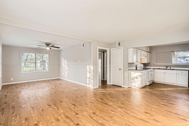 unfurnished living room featuring beamed ceiling, light wood-type flooring, ceiling fan, and sink