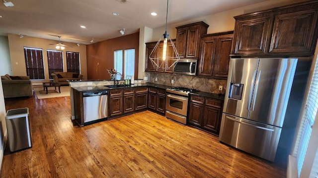 kitchen featuring kitchen peninsula, backsplash, stainless steel appliances, sink, and pendant lighting