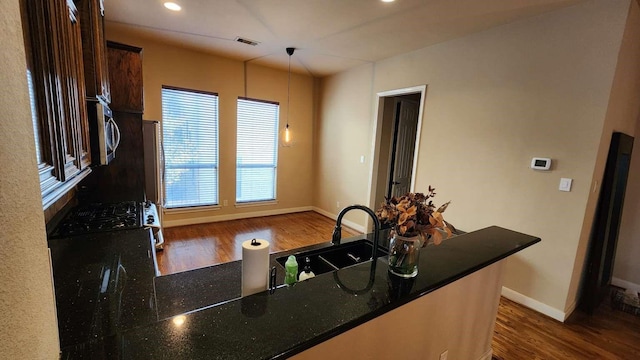 kitchen with dark brown cabinetry, hanging light fixtures, dark hardwood / wood-style flooring, kitchen peninsula, and black range