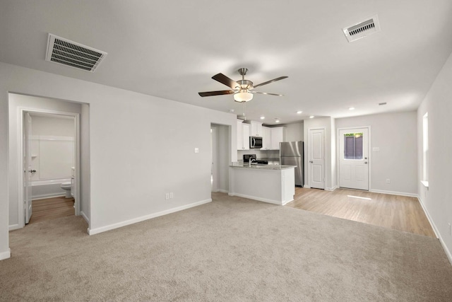 unfurnished living room featuring ceiling fan, light colored carpet, and sink