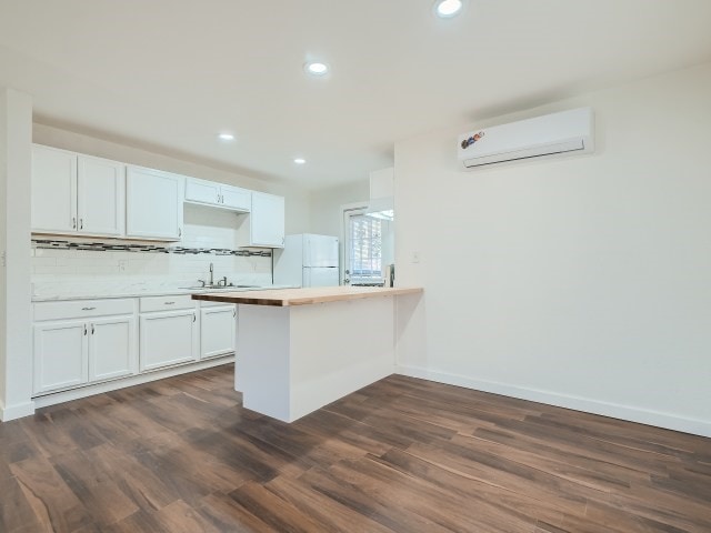 kitchen featuring white cabinets, dark hardwood / wood-style floors, white refrigerator, and an AC wall unit