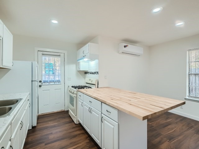 kitchen featuring white cabinets, a wall unit AC, and white gas stove