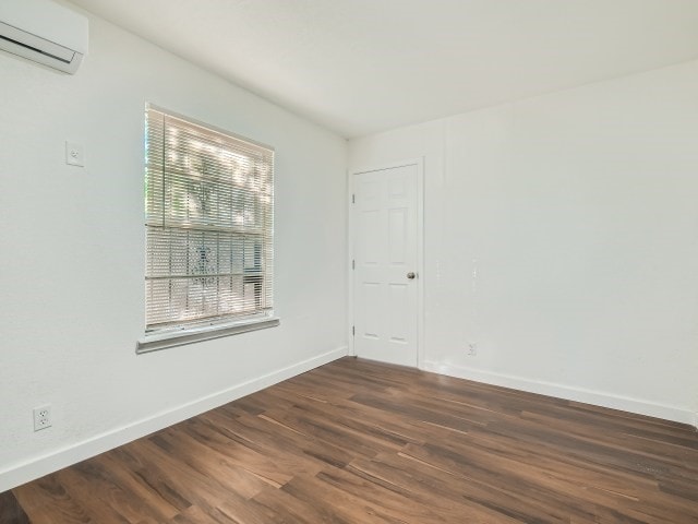 spare room with an AC wall unit, a wealth of natural light, and dark wood-type flooring