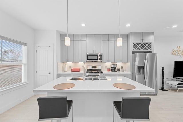 kitchen featuring a kitchen bar, stainless steel appliances, decorative light fixtures, a center island with sink, and gray cabinets