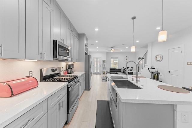 kitchen with ceiling fan, stainless steel appliances, light stone counters, an island with sink, and decorative light fixtures