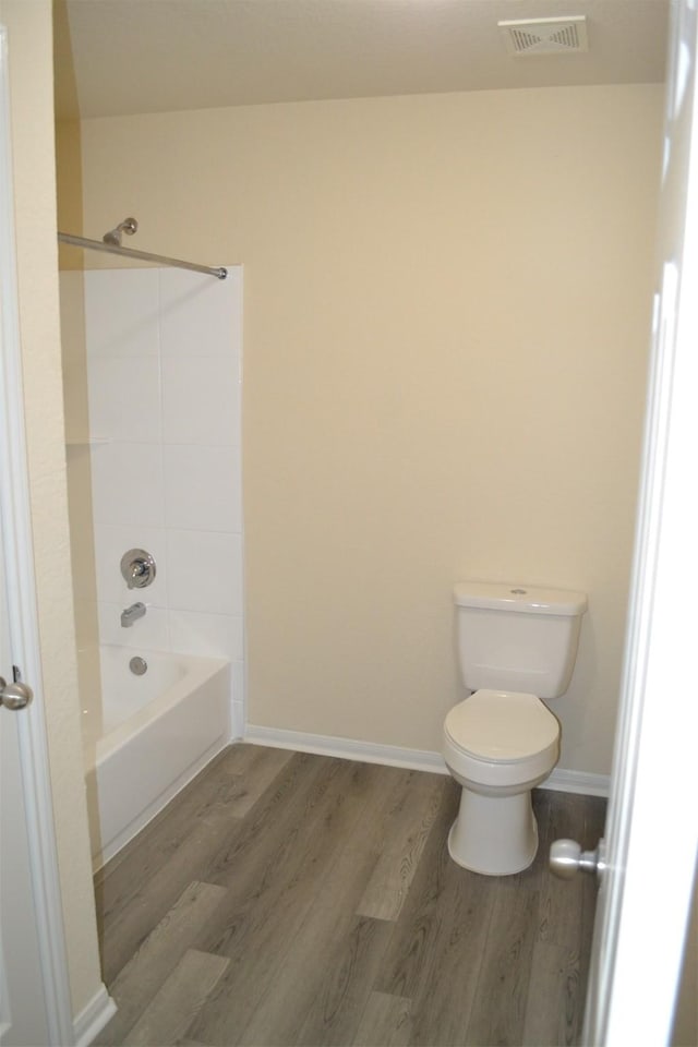 bathroom featuring shower / washtub combination, hardwood / wood-style floors, and toilet