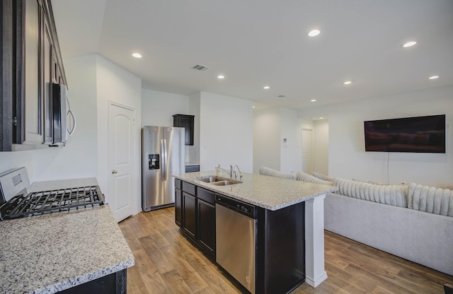 kitchen with a kitchen island with sink, sink, light hardwood / wood-style flooring, light stone countertops, and appliances with stainless steel finishes