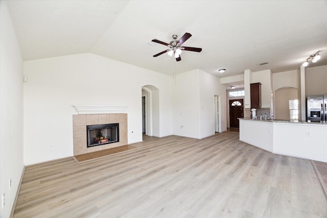 unfurnished living room featuring ceiling fan, vaulted ceiling, a tile fireplace, and light hardwood / wood-style flooring