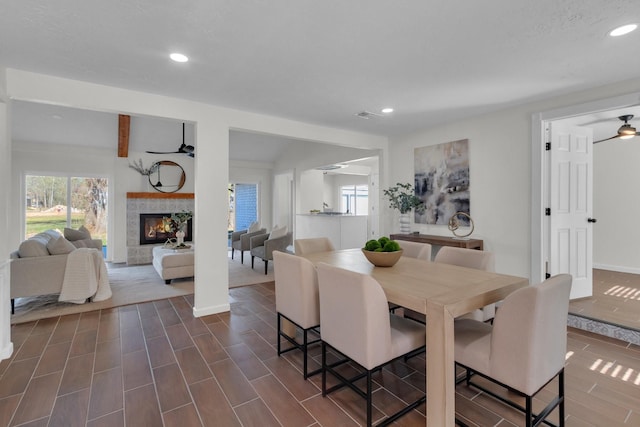 dining room featuring ceiling fan, a healthy amount of sunlight, and a tiled fireplace