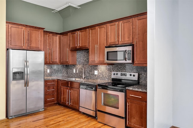 kitchen with sink, tasteful backsplash, dark stone countertops, appliances with stainless steel finishes, and light wood-type flooring