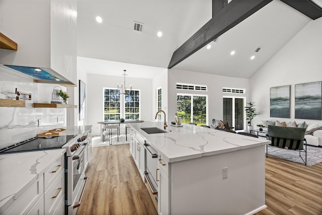 kitchen with a center island with sink, white cabinets, high end range, and sink