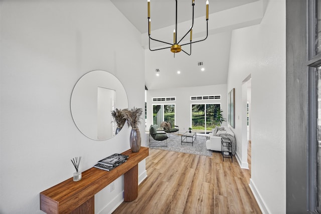 corridor with a high ceiling, an inviting chandelier, and light hardwood / wood-style flooring