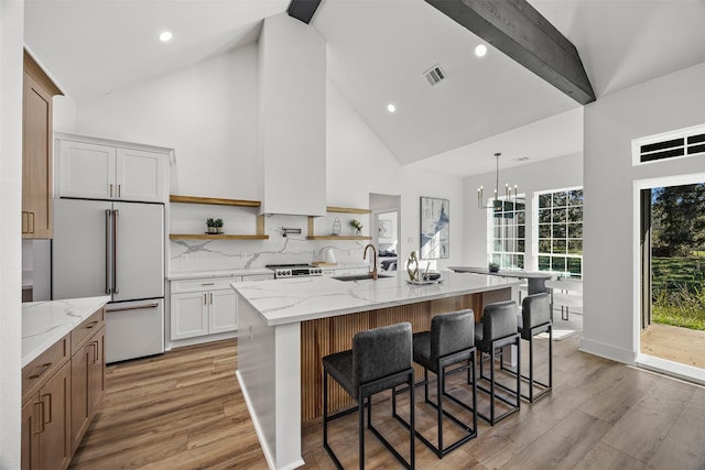 kitchen with a spacious island, sink, light stone countertops, high end fridge, and white cabinetry