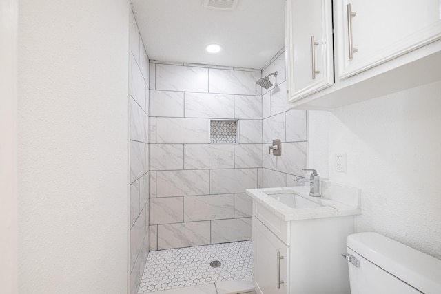 bathroom with vanity, toilet, and a tile shower