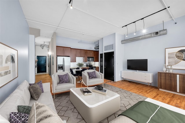 living room featuring light wood-type flooring, rail lighting, and a high ceiling