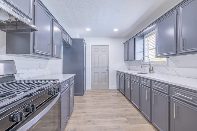 kitchen featuring gas stove, light stone countertops, sink, light hardwood / wood-style floors, and a textured ceiling