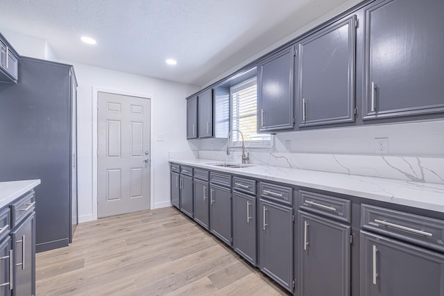 kitchen with gray cabinets, light hardwood / wood-style floors, light stone counters, and sink