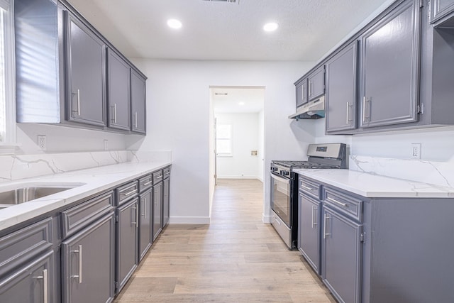 kitchen with light stone countertops, stainless steel gas range oven, and gray cabinetry