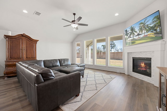 living room featuring wood-type flooring, vaulted ceiling, a stone fireplace, and ceiling fan