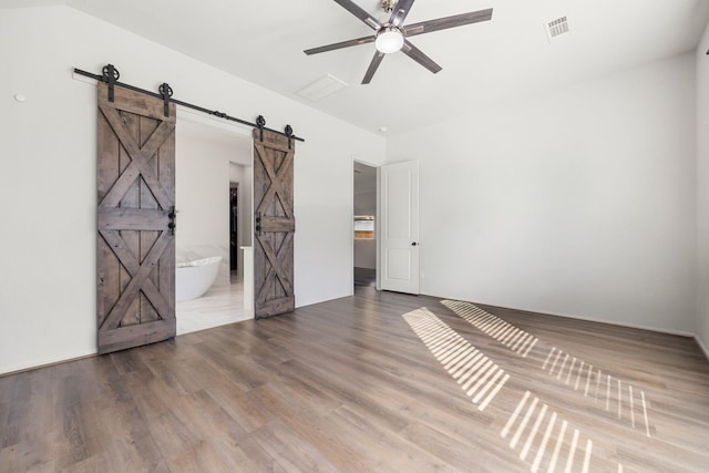 unfurnished room with a barn door, ceiling fan, and hardwood / wood-style floors