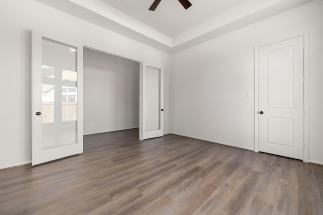 unfurnished bedroom featuring french doors, a raised ceiling, ceiling fan, and dark wood-type flooring