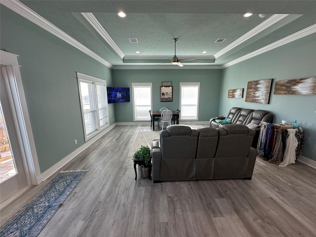 living room with hardwood / wood-style floors, ceiling fan, ornamental molding, and a tray ceiling