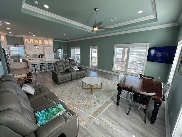 living room featuring a tray ceiling, ceiling fan, light hardwood / wood-style floors, and ornamental molding
