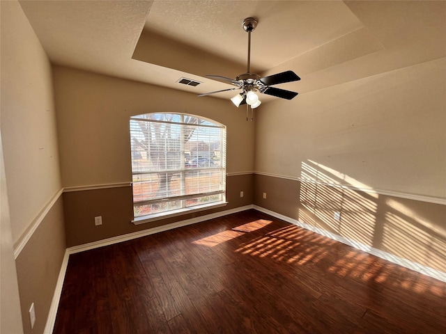 unfurnished room featuring a raised ceiling, ceiling fan, a textured ceiling, and dark hardwood / wood-style flooring