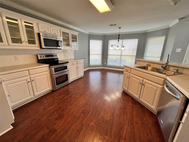 kitchen with sink, stainless steel appliances, ornamental molding, white cabinets, and decorative light fixtures